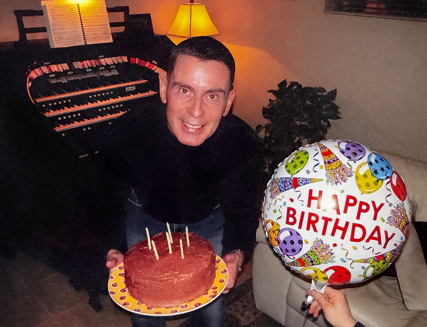 Will smiling behind a 65th birthday cake and birthday balloon