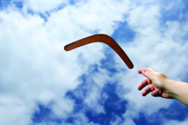 Hand tossing a boomerang into a blue sky