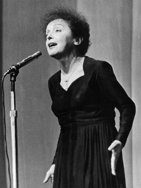 Black-and-white photo of Edith Piaf leaning forward towards a microphone