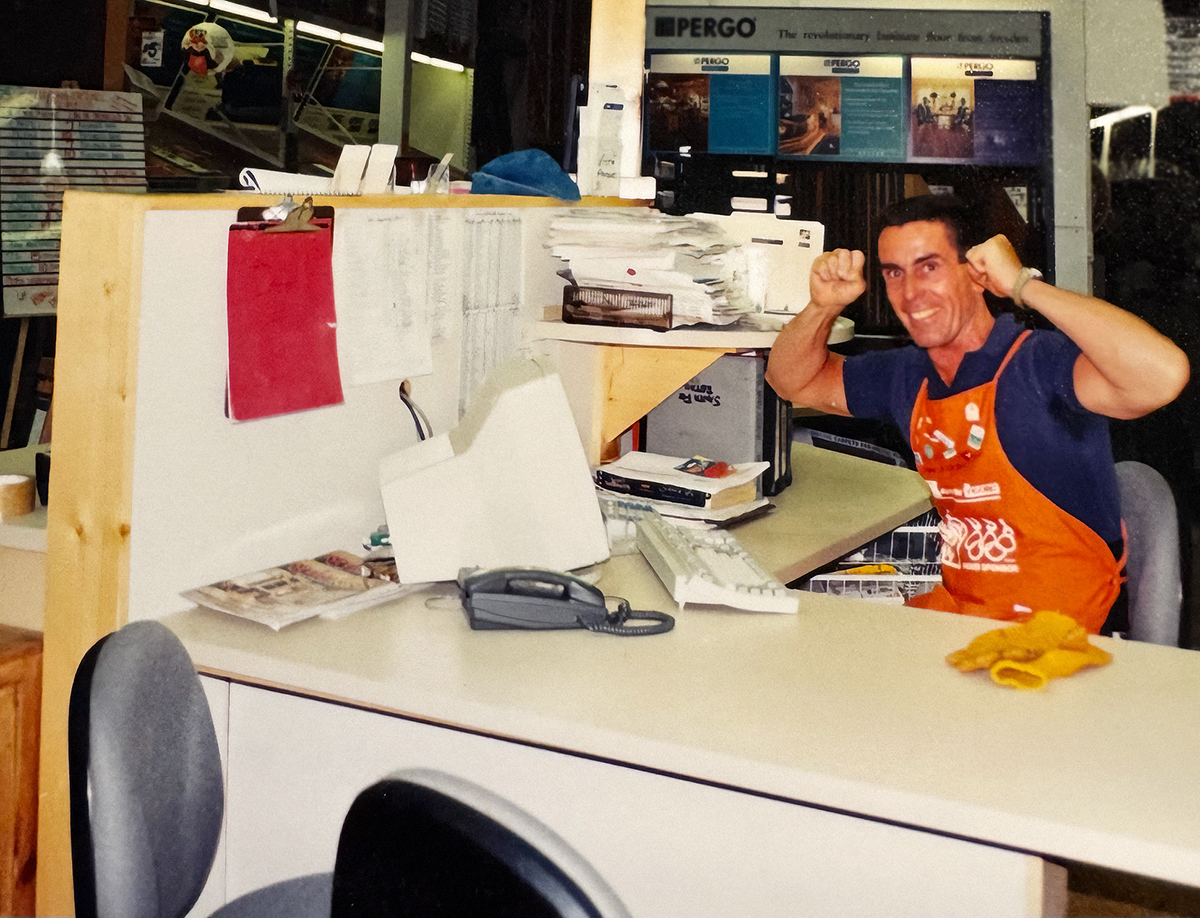 Will in excited pose sitting at a desk in orange Home Depot apron